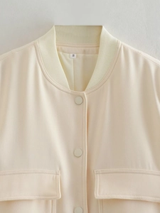 Detail of a cream bomber jacket showing the ribbed collar, S size tag, and smooth fabric