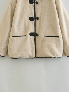 Détail du manteau en fausse fourrure crème avec bordure noire et boutons à bascule