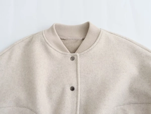 Detailansicht der beigen Wolljacke mit geripptem Kragen und metallischen Druckknöpfen