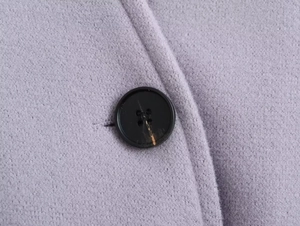 Détail macro d'un bouton noir à quatre trous sur le tissu en laine violet de la veste