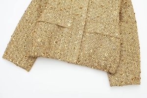 Detail shot of golden sequin tweed jacket with intricate metallic weave and elegant finish