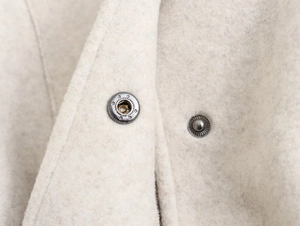 Detail eines Metalldruckknopfs mit Sternenmuster auf cremefarbenem Wolljackenstoff
