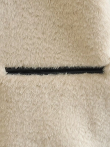 Détail macro de la texture fausse fourrure crème et contraste de poche noire sur manteau