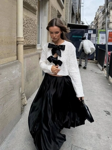 Detalle de chaqueta de tweed blanca con lazos de satén negro y falda larga de satén liso