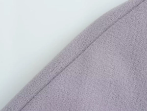 Gros plan sur la texture douce du tissu polaire lilas et les coutures de la veste