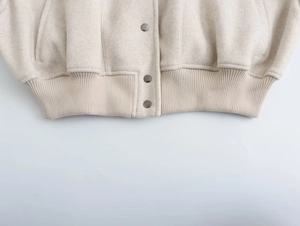 Detail der silbernen Metallknöpfe und des Rippsaums der dicken cremeweißen Wolljacke