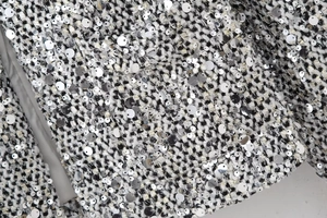 Close-up detail of silver sequins and black and white tweed fabric on women blazer