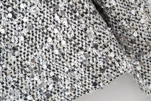 Close-up detail of silver sequins and black and white tweed fabric texture on luxury blazer