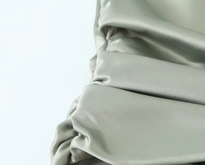 Detailed macro view of mint green satin fabric featuring elegant pleated texture and silk gloss