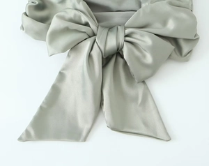 Detailed view of sage green satin top featuring a large bow and silky fabric texture