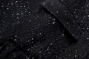 Detailed macro shot of black tweed fabric featuring shimmering silver sequins and texture