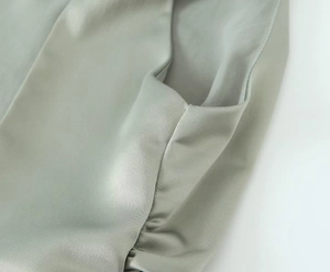 Detail of light green satin top showing delicate ruching and premium fabric texture