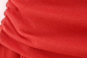 Close-up of red knitted fabric texture with soft fibers and elastic pleated details