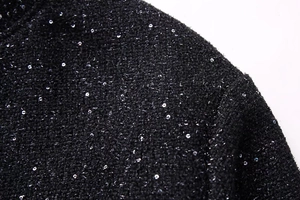 Macro shot of black tweed fabric with shimmering silver sequins on a standing collar jacket