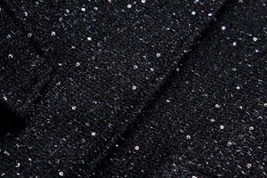 Macro shot of black tweed fabric with shimmering silver sequins on a textured jacket