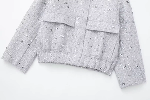 Detailed close-up of grey tweed jacket fabric with shimmering silver sequins and flap pockets