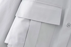 Détail macro d'une chemise gris clair montrant le tissu sergé et la poche à rabat