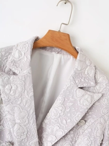 Detailed macro view of textured floral jacquard fabric and silver crest button on blazer