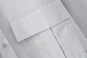 Détail de chemise en sergé gris clair montrant la poche à rabat et la couture précise