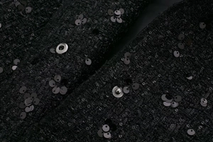 Detail of black tweed jacket featuring intricate sequins and silver metallic snap buttons