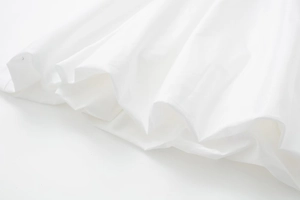 Détail de l'ourlet de jupe midi blanc pur avec plis ondulés et texture coton nette