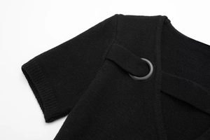 Detail view of black knit dress neckline featuring crisscross straps and matte metal rings