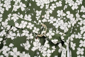 Detail of dark green floral dress featuring white flower patterns and golden D-ring belt