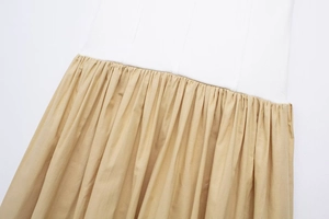 Detail of waist stitching and pleated khaki fabric on a white panel dress