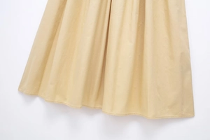 Detailed close-up of pale yellow pleated dress fabric with a fine woven texture and drape