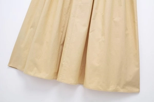 Detailed close-up showing the pleated hem and fine stitching of a beige cotton skirt