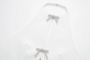 Detail eines weißen Halterneck-Tops mit zwei silbernen Strass-Schleifen-Dekorationen