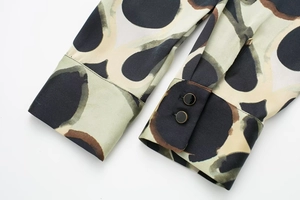 Détail du poignet en satin avec boutons noirs bordés d'or et imprimé géométrique