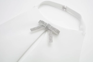 Detail eines weißen Halterneck-Tops mit einer funkelnden Strass-Schleifenschnalle als Akzent
