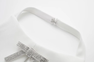 Dettaglio macro del collo all'americana bianco con gancio argento e fiocco di strass