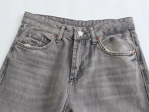 Detail of waist area on grey washed denim wide leg pants with metal button and rivets