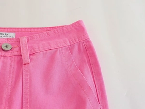 Detail of pink denim pants showing metallic button, belt loops and twill texture
