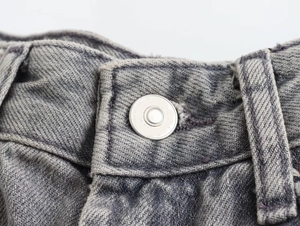 Close-up of silver metal button and reinforced belt loops on grey washed denim jeans