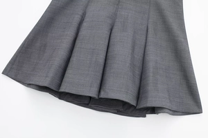 Detail shot of grey pleated dress showing textured fabric weaving and neat hemline stitching