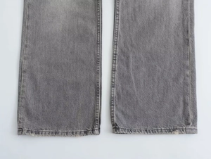 Detail of the distressed hem and double stitching on these gray wide-leg denim jeans