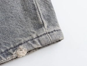 Macro shot of grey washed denim fabric featuring distressed hem and contrast stitching