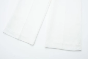 Detailed view of white wide-leg trousers hem with precise pleats and fine stitching finish