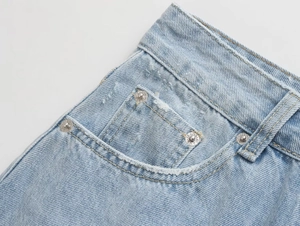 Detail of high-waisted light blue denim shorts featuring washed fabric and metal rivets
