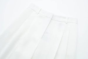 Detail of waist design on white pleated wide-leg trousers with belt loops and clean stitching