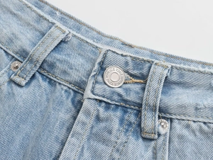 Close-up of light blue denim shorts featuring silver metal button and waist stitching details