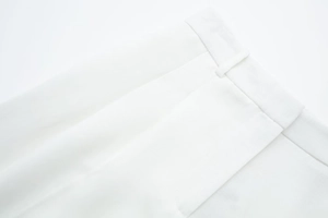 Detailed macro view of white trousers showing waist loops and precise pleating texture