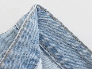 Detail shot of light blue denim shorts with orange stitching and twill fabric texture