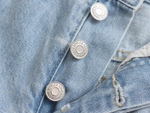 Detailed close-up of light blue denim shorts featuring a triple silver button fly closure