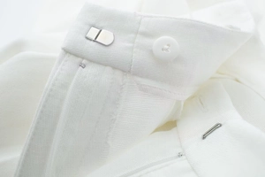 Detail of white trousers showing waist closure with a metal hook and button on twill fabric