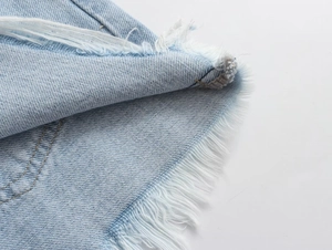 Close-up of frayed raw hem and fringe details on light blue denim shorts for women