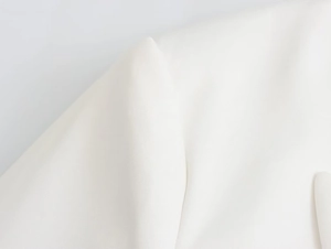 Detailed close-up showing the premium woven texture and stitching of white blazer shoulder